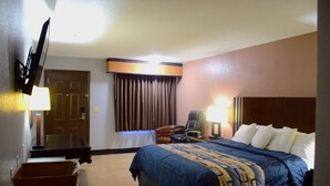Ein Hotelzimmer mit Bett, Schreibtisch, Stuhl, Fernseher und einem Fenster mit Vorhängen.
