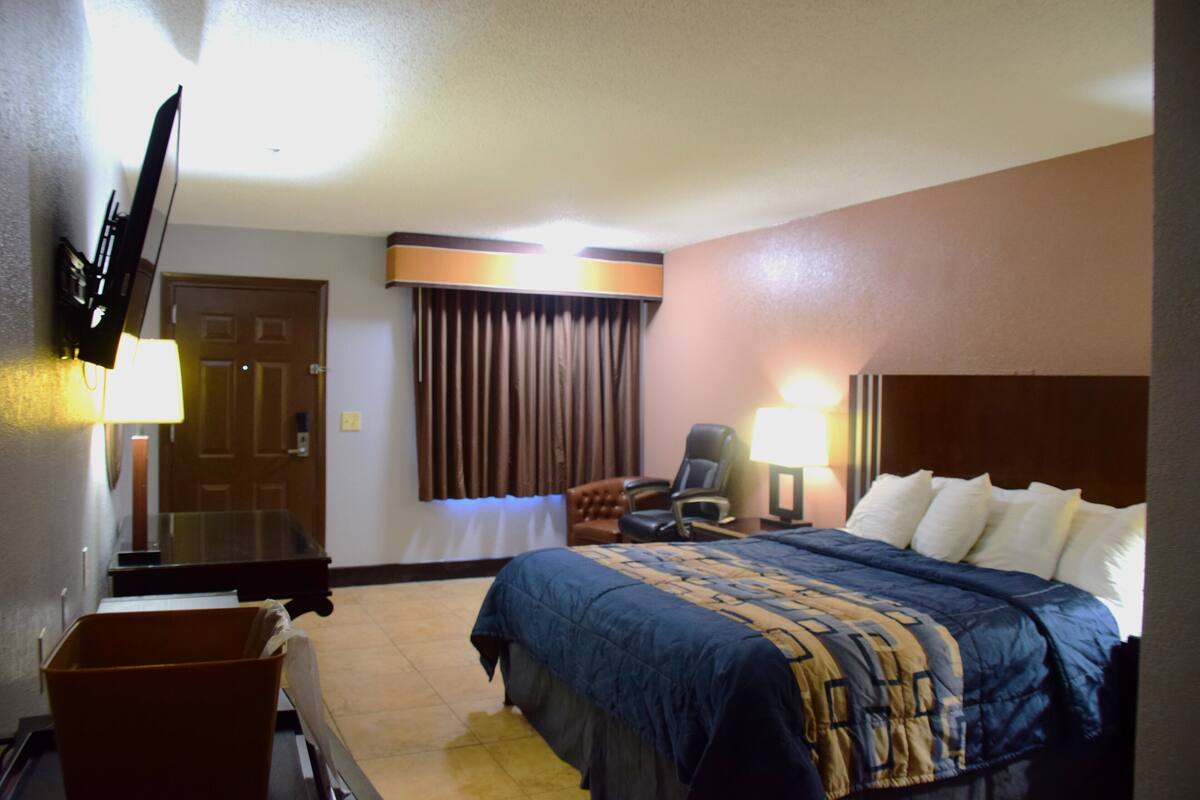 A hotel room with a bed, a desk, a chair, a TV, and a window with curtains.