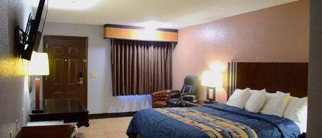 A hotel room with a bed, a desk, a chair, a TV, and a window with curtains.