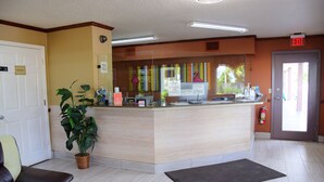 Ein Empfangsbereich mit einer Rezeption, einer Pflanze, einem Feuerlöscher und einem Hinweisschild für den Notausgang.