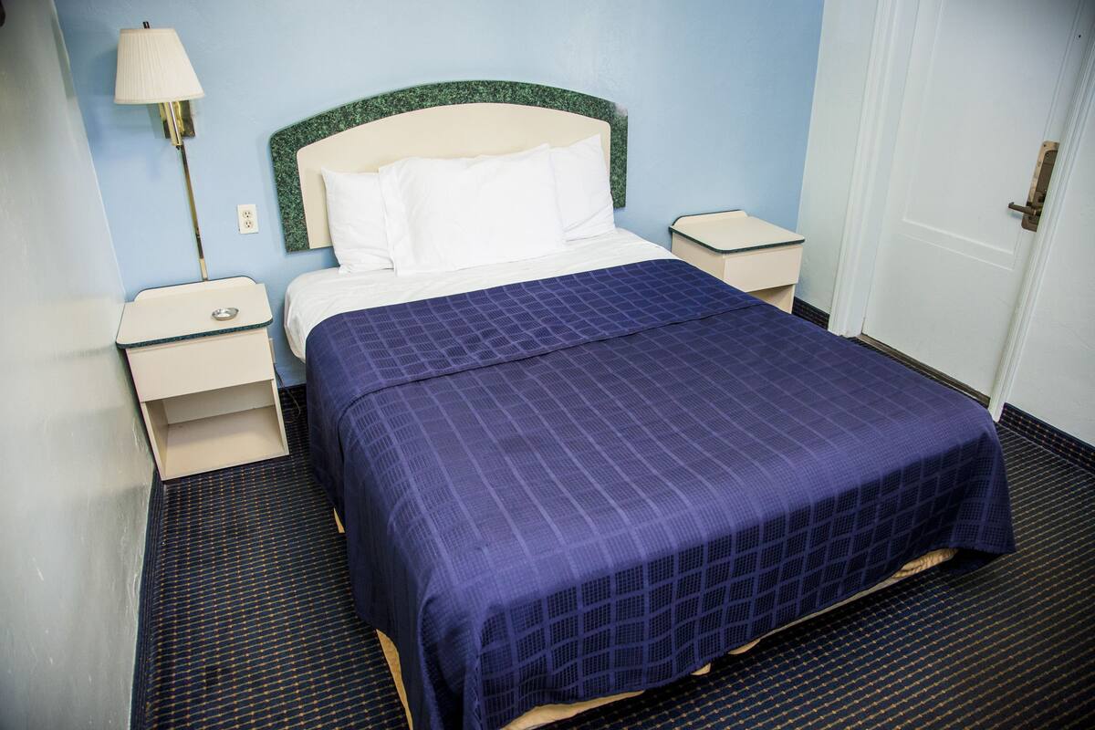 A hotel room with a bed, nightstands, a lamp, and a door.