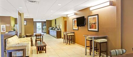 A hotel lobby with a reception desk, seating area, and a kitchenette.