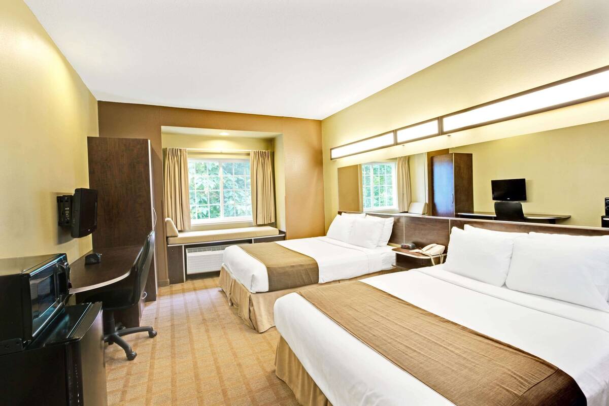 A hotel room with two beds, a desk with a computer, a TV, and a window with curtains.