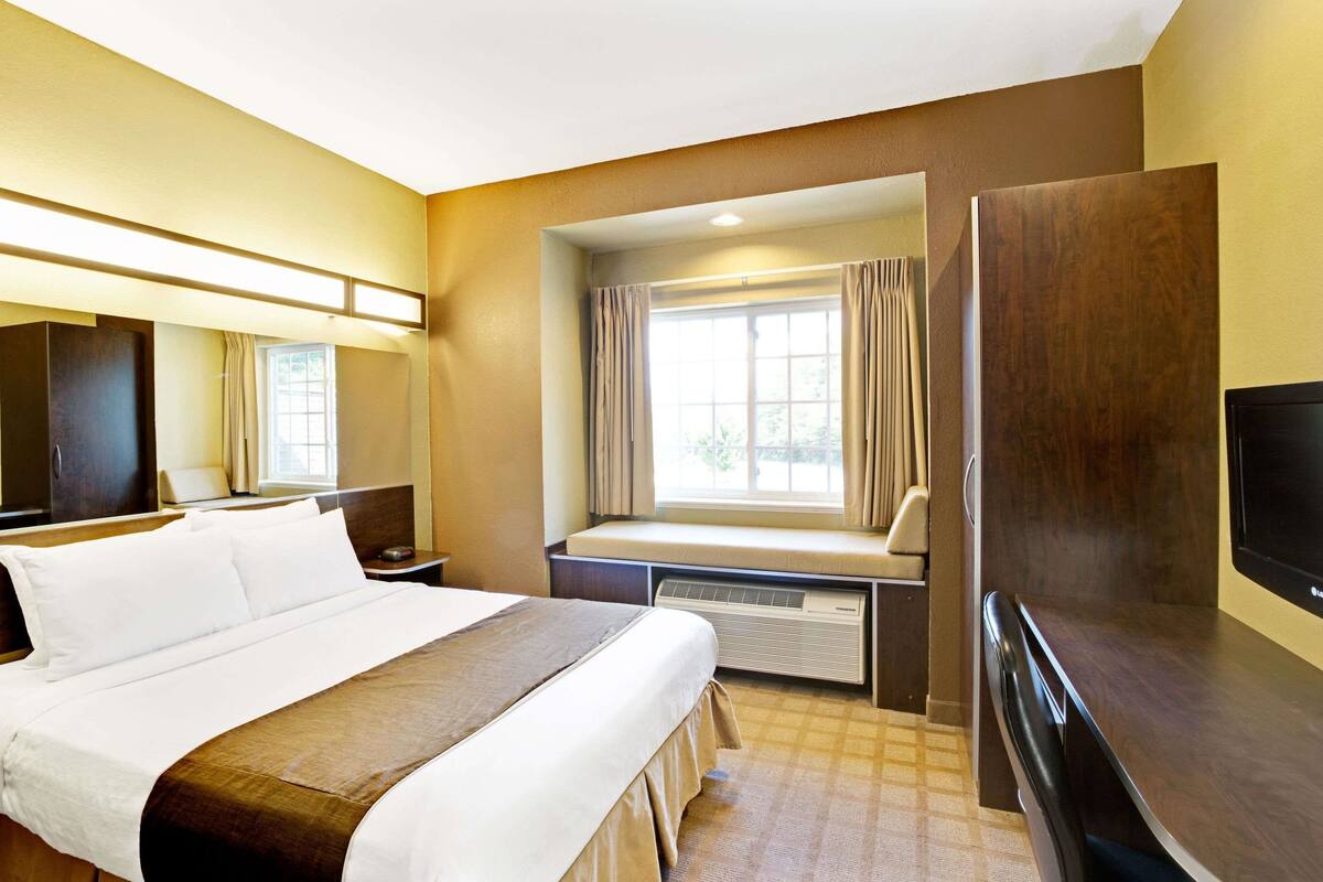 A hotel room with a large bed, a desk with a chair, a television, and a window with curtains.
