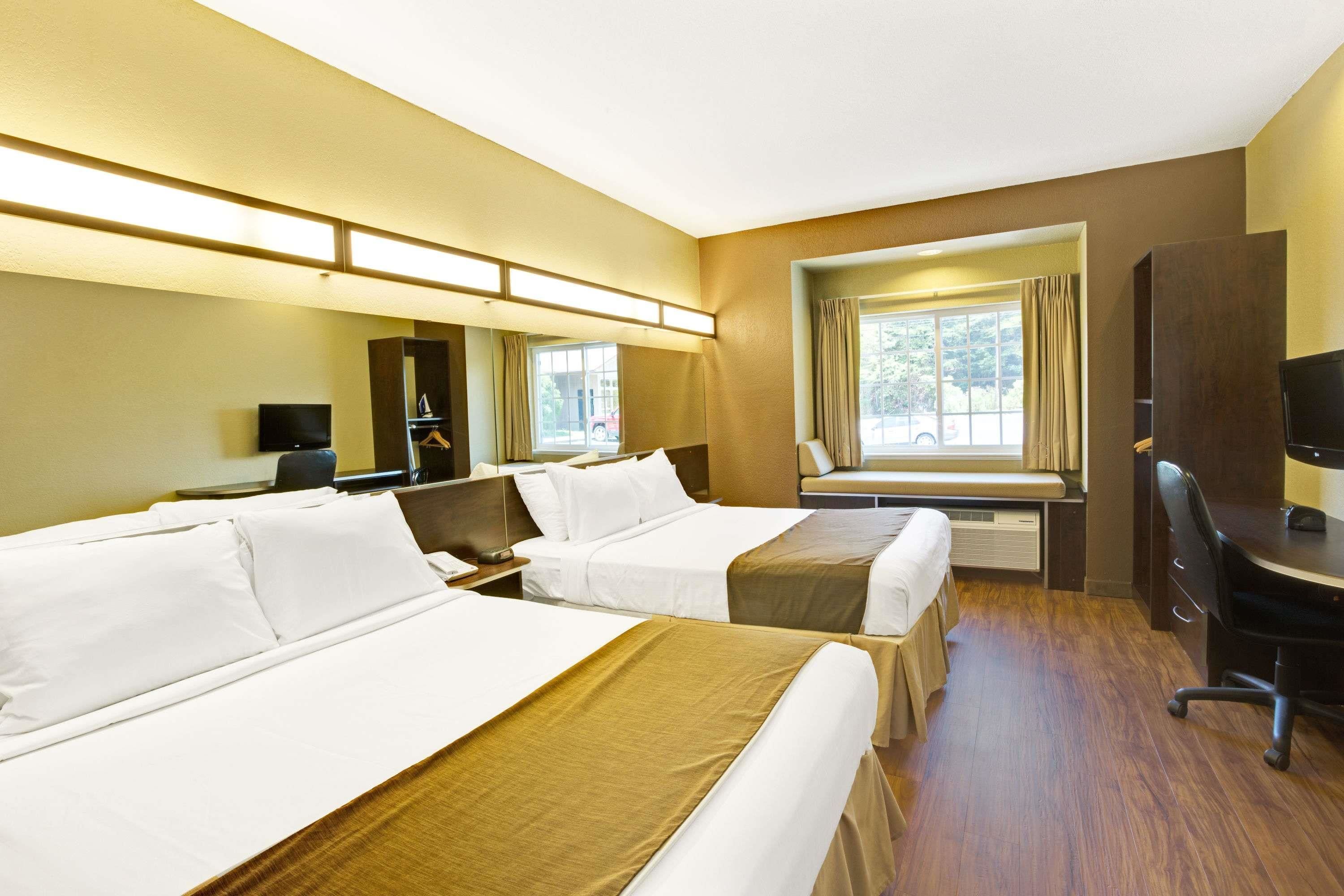 A hotel room with two beds, a desk, a chair, a TV, and a window with curtains.