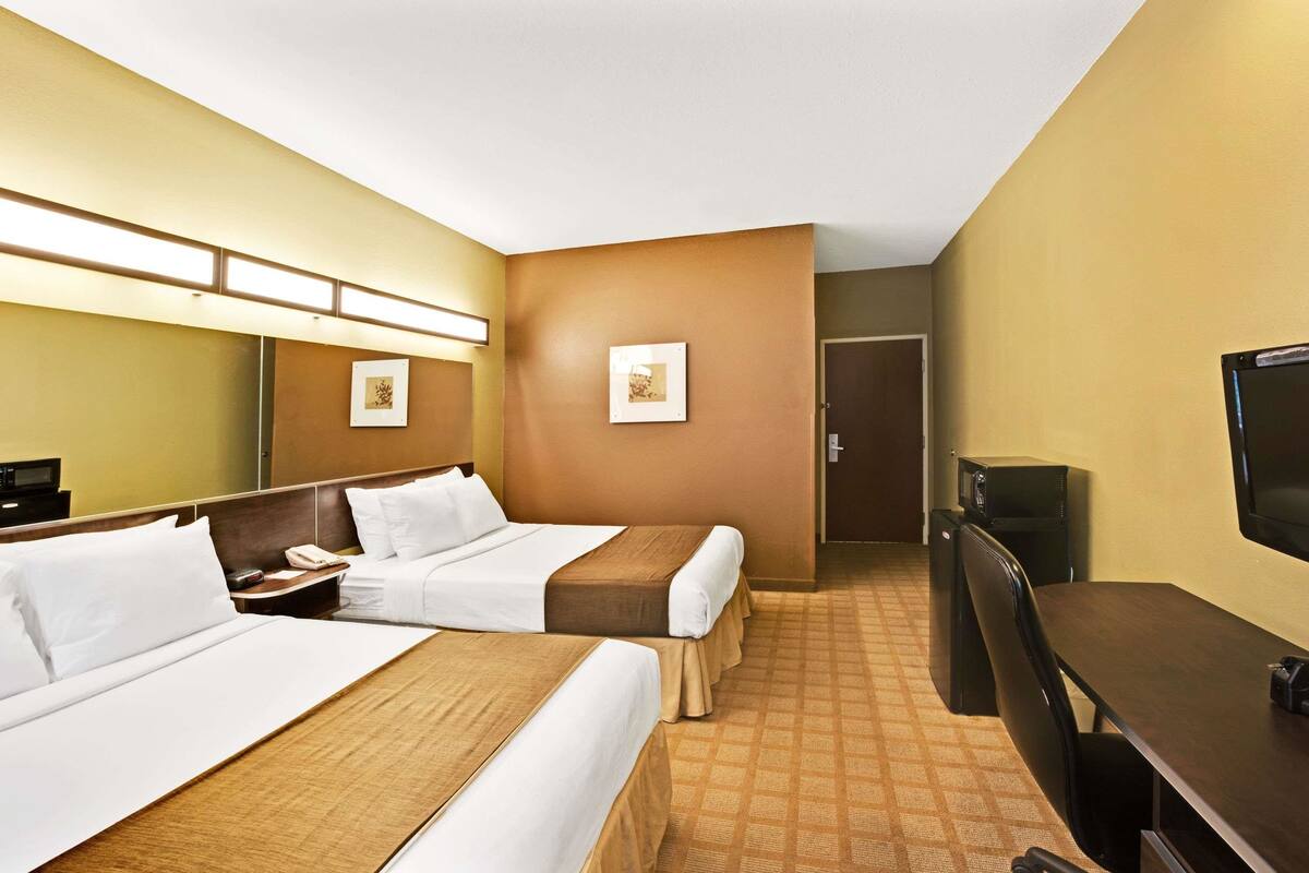 A hotel room with two beds, a desk, a television, and a door.
