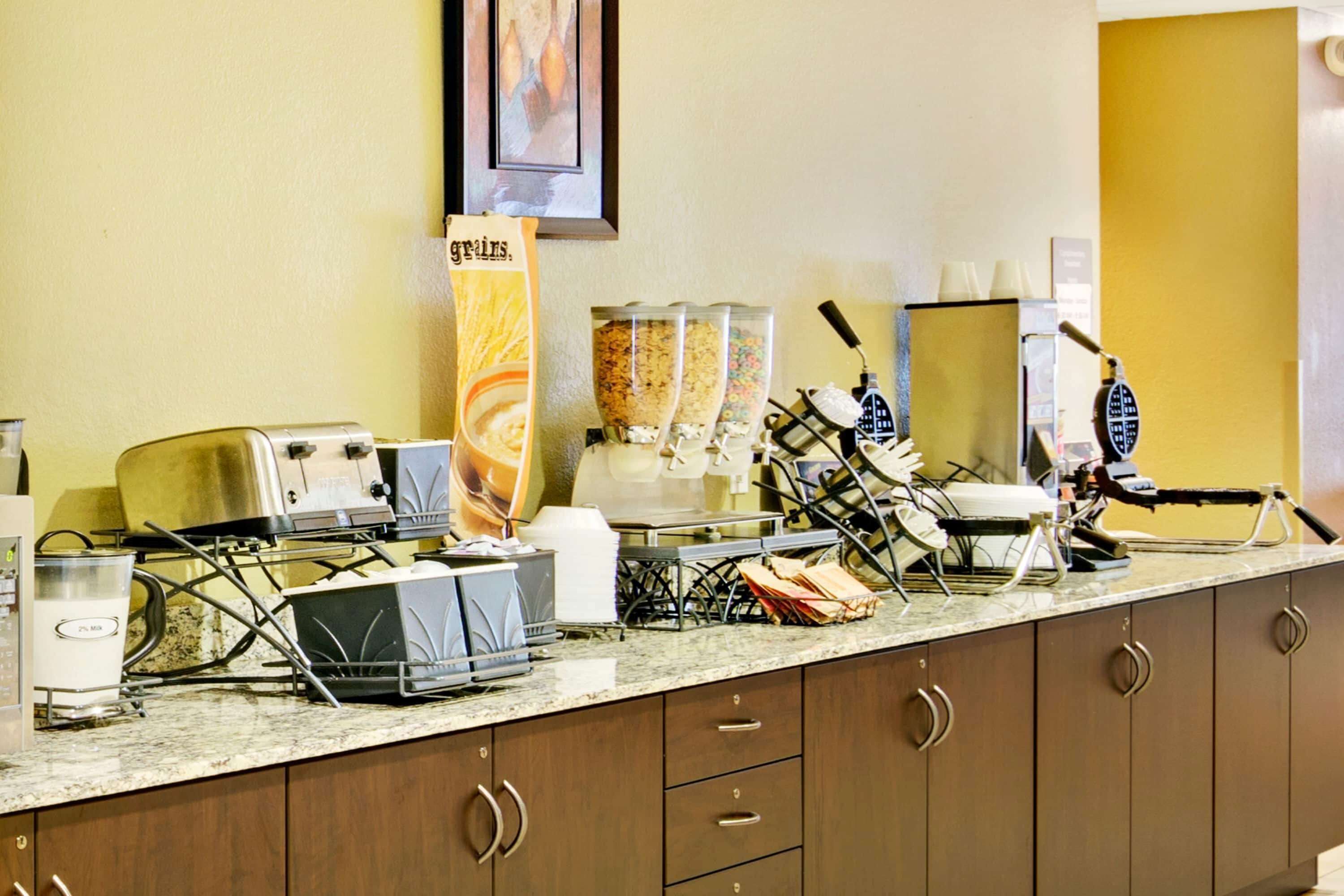 A breakfast bar with various food items and appliances, including a coffee maker, a waffle maker, and a blender.