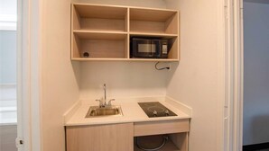 Una kitchenette compacta con un lavamanos de acero inoxidable, una placa de cocción por inducción negra y un microondas sobre una repisa de madera.