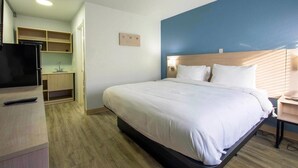 Habitación de hotel con cama, televisor, escritorio y una pequeña cocina.