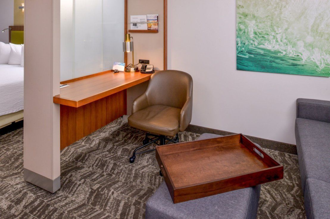Une chambre d’hôtel avec un lit, un bureau et une chaise, une petite table et un canapé gris.