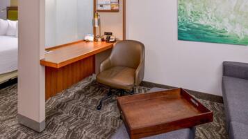 Une chambre d’hôtel avec un lit, un bureau et une chaise, une petite table et un canapé gris.