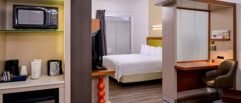 A hotel room with a bed, a desk, a microwave, a small refrigerator, and a television.
