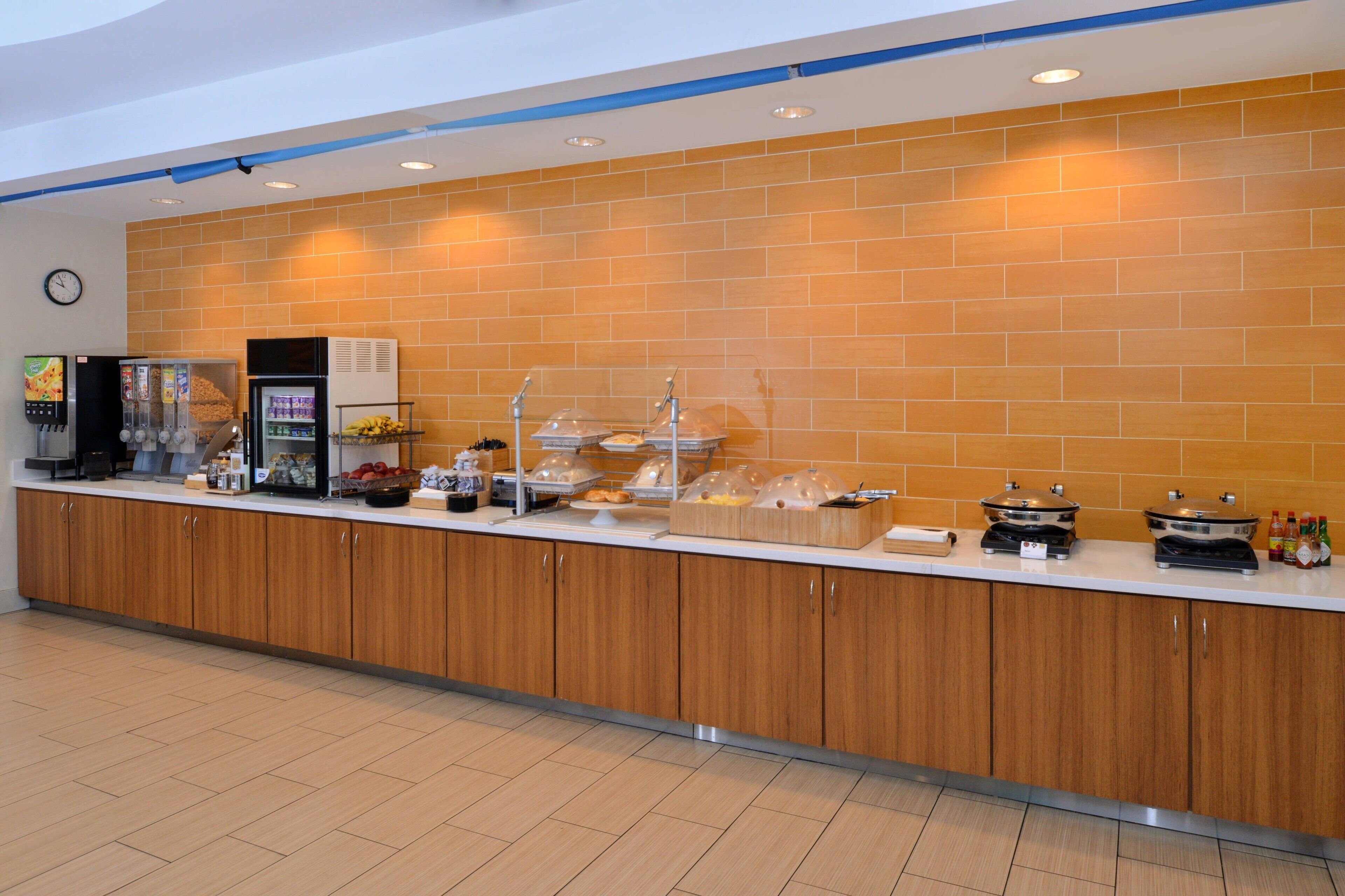 A buffet counter with a variety of food items, a beverage dispenser, and a clock on the wall.