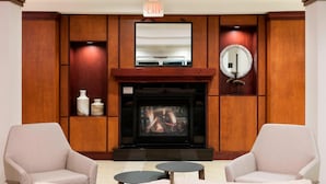 A lobby with a fireplace, two armchairs, a small table, and a mirror. - Fairfield by Marriott Inn & Suites Austin Parmer/Tech Ridge (Austin)