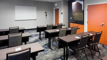 A conference room with tables, chairs, a projector screen, and a door with a view of a building.