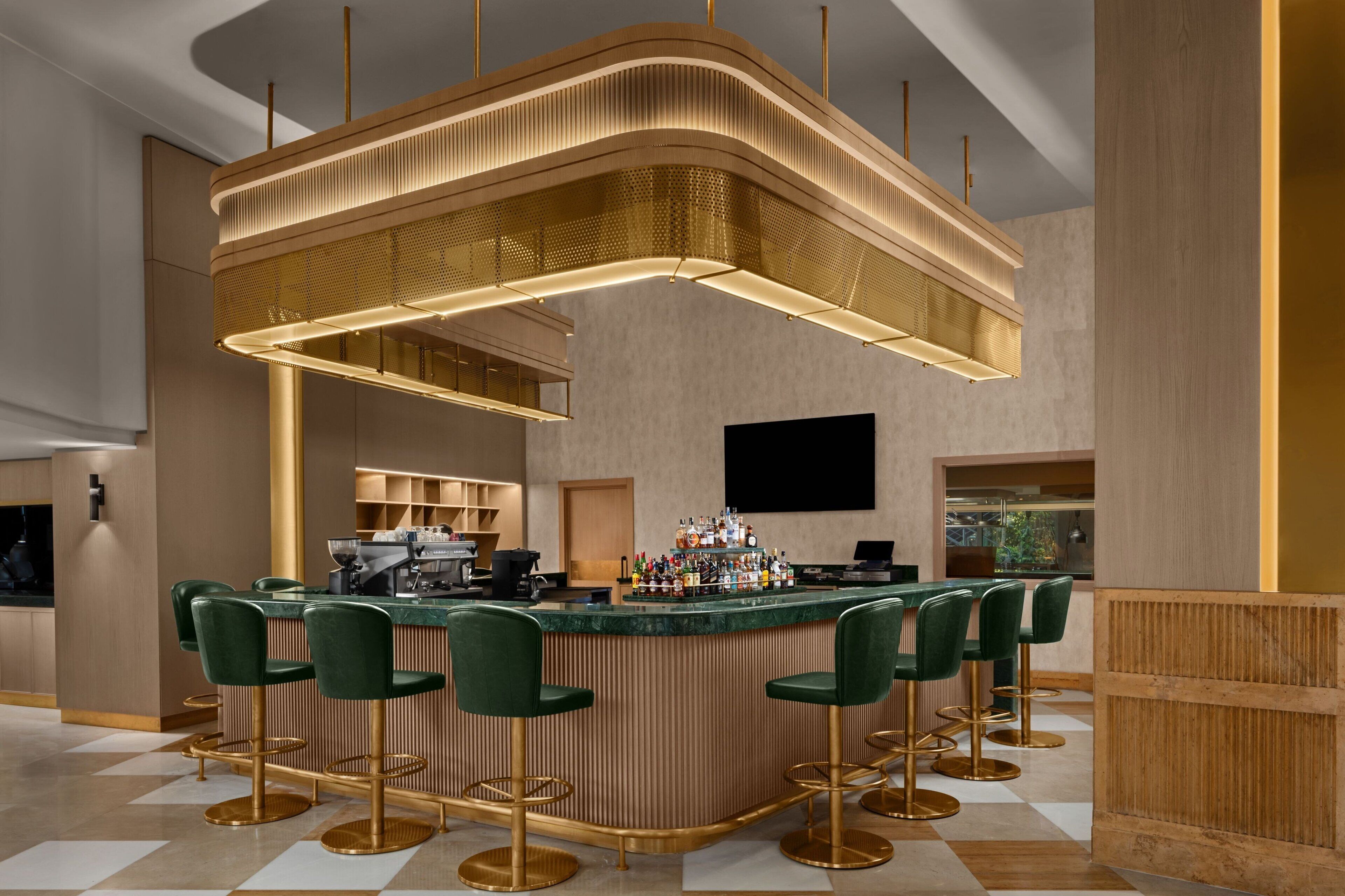 A modern bar area with a curved bar, green bar stools, and a unique overhead lighting fixture.