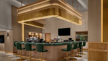 A modern bar area with a curved bar, green bar stools, and a unique overhead lighting fixture.