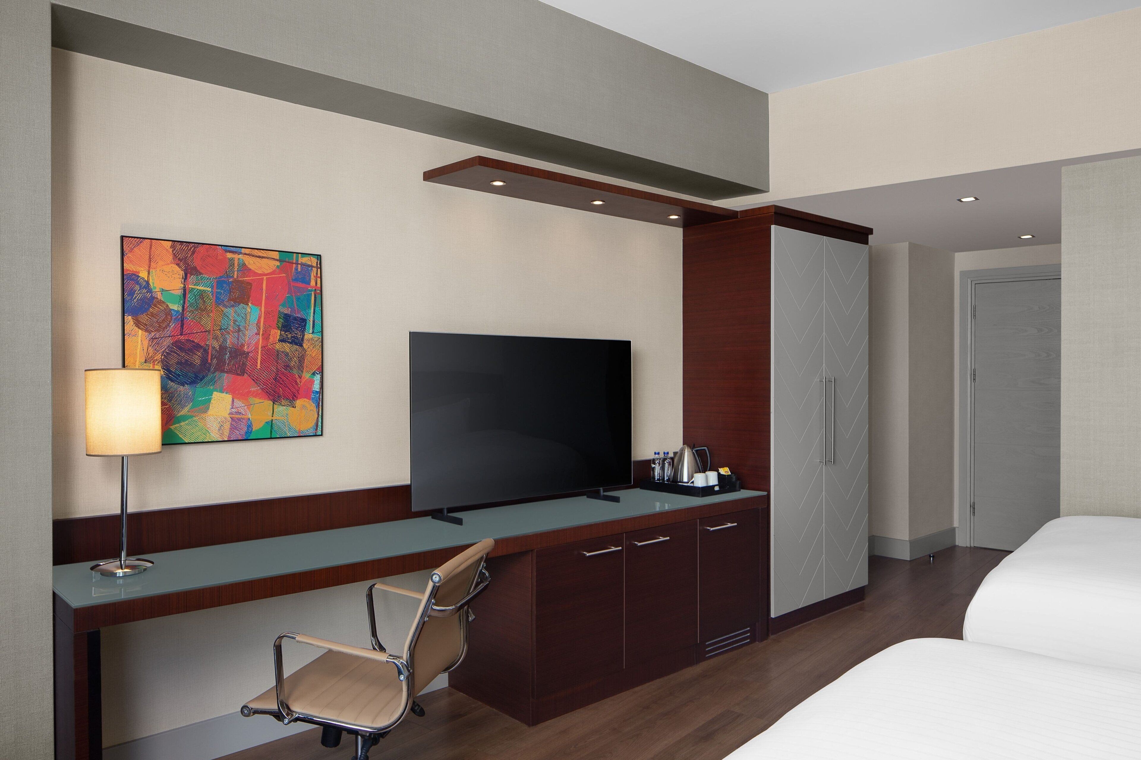 Een hotelkamer met een flatscreen televisie, een bureau met lamp, een stoel, een bed en een kledingkast.