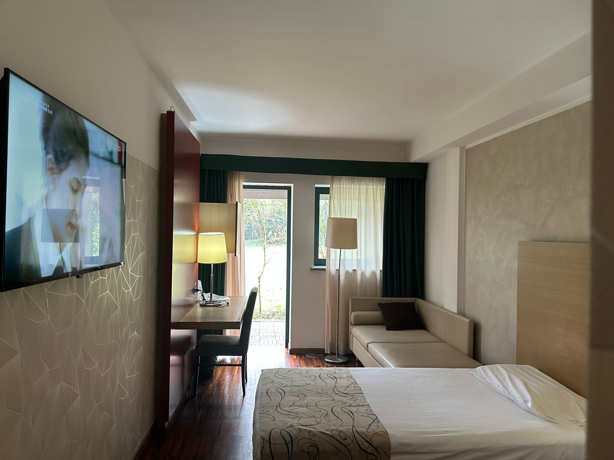 Een hotelkamer met een bed, een bureau, een stoel, een televisie en een raam met gordijnen.