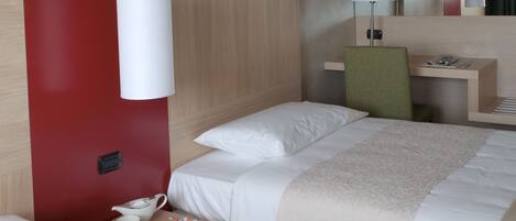 Een hotelkamer met twee bedden, een bureau, een stoel en een nachtkastje met een lamp.