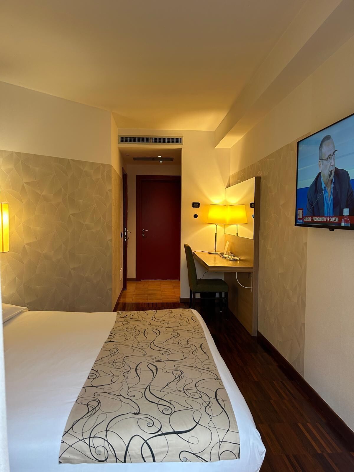Una habitación de hotel con cama, escritorio, silla, televisor y puerta.
