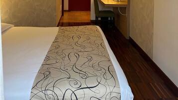 Una habitación de hotel con cama, escritorio, silla, televisor y puerta.