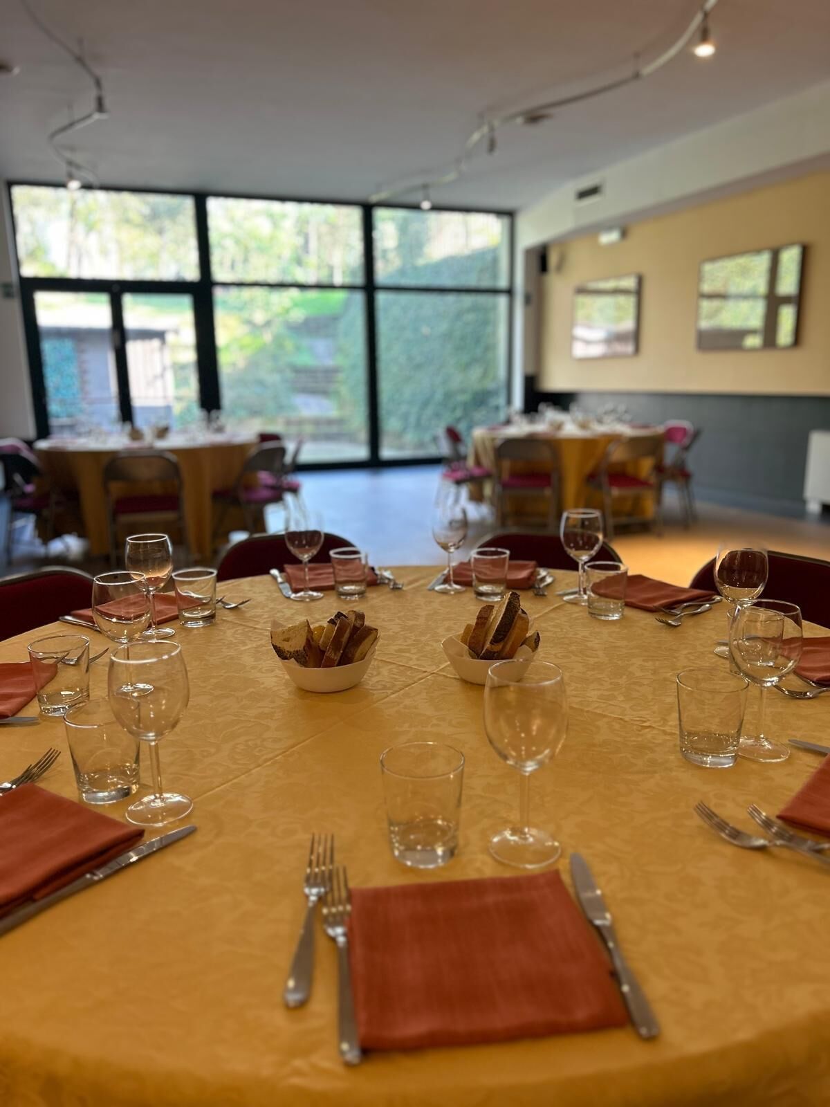 Comedor con mesas redondas dispuestas para una comida, cada una con copas de vino, vasos de agua y cubiertos.
