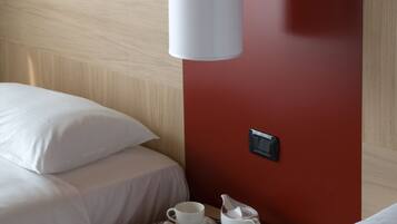 Habitación de hotel con cabecera de madera, pared de acento roja, mesita de noche con una taza, un libro y un control remoto.