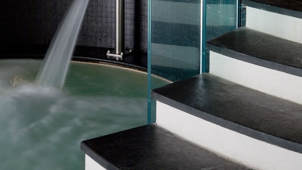 A modern bathroom with a glass-enclosed shower, a bathtub, and a set of dark steps leading to a tiled area.