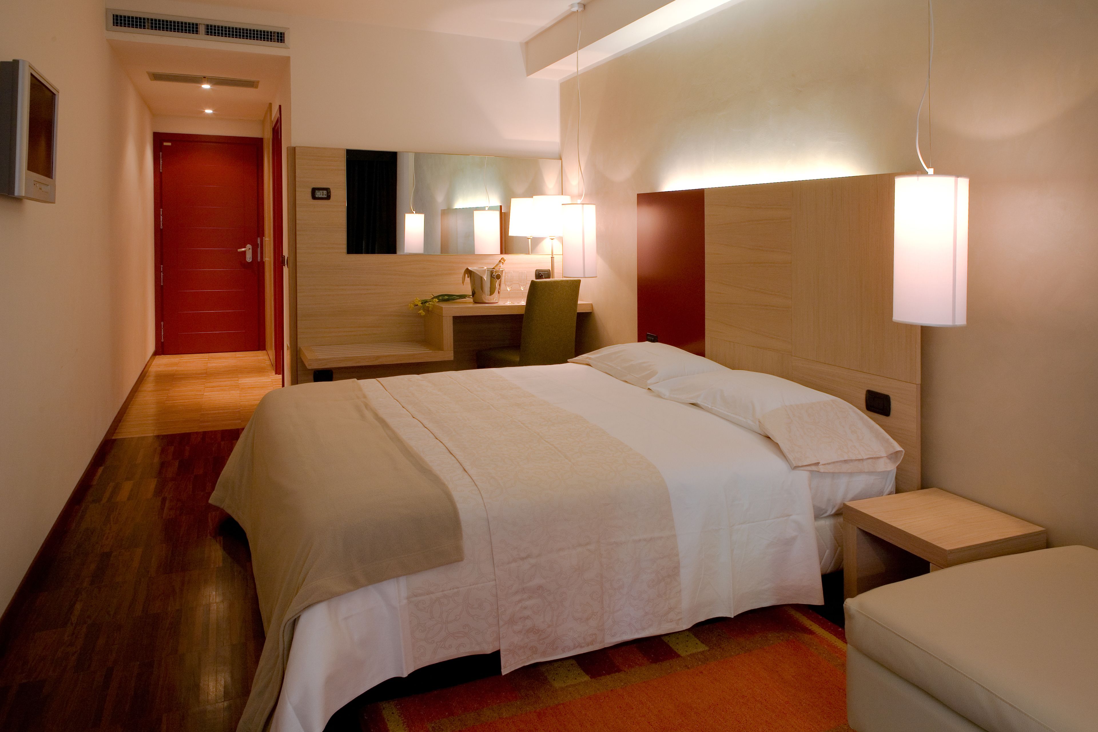 A hotel room with a bed, bedside table, nightstand, desk, chair, and a mirror.