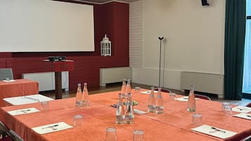 A conference room with a long table, red chairs, water bottles, and a projector screen.
