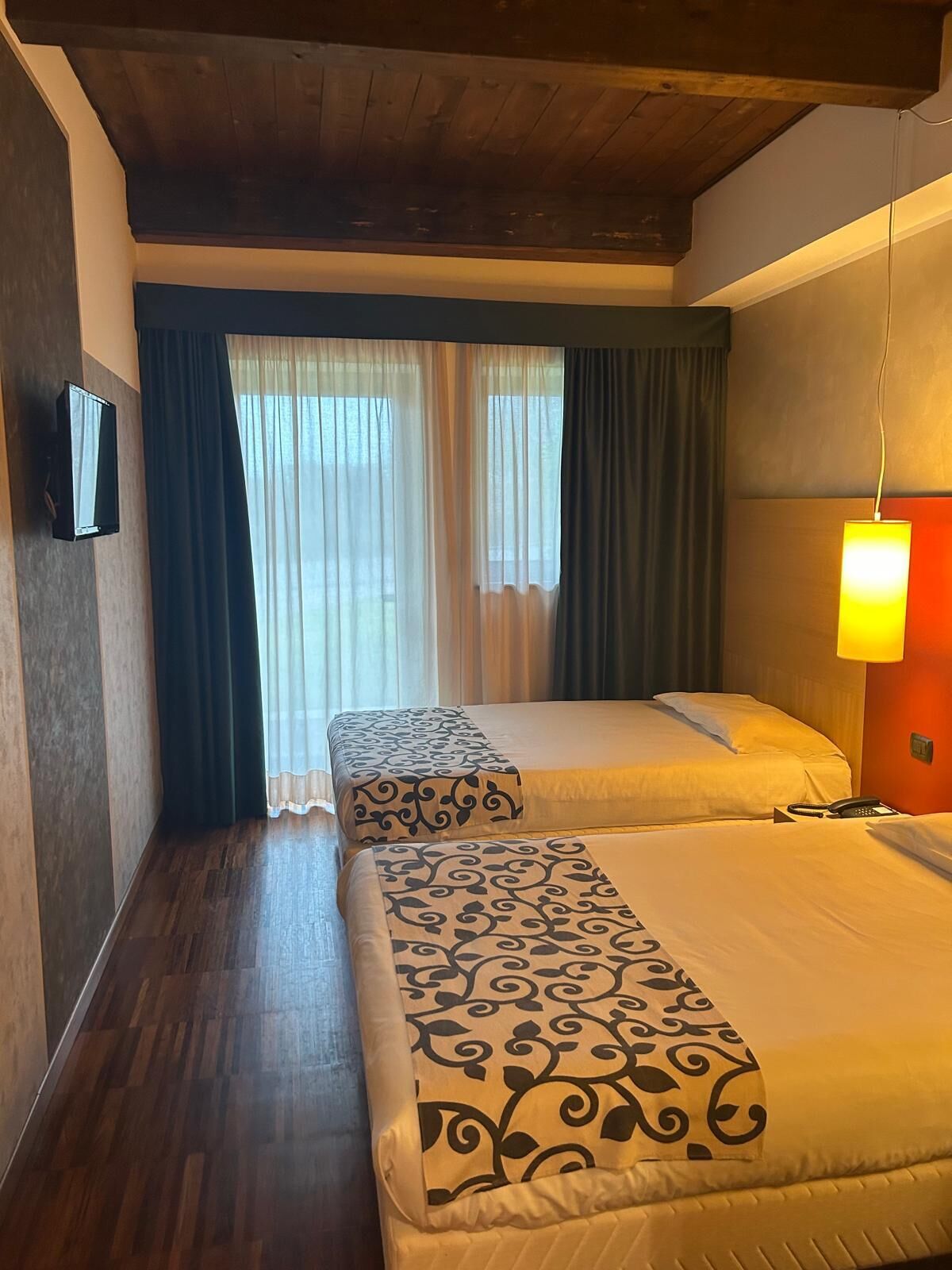 Habitación de hotel con dos camas, un televisor en la pared y una lámpara en la mesita de noche.