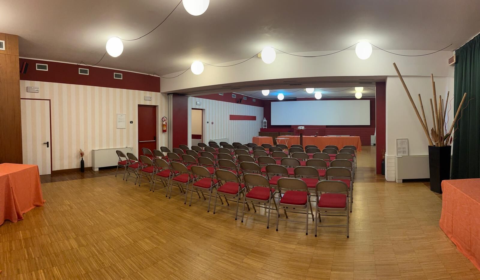 Un salón de conferencias con filas de sillas, una pantalla de proyector y un escenario.