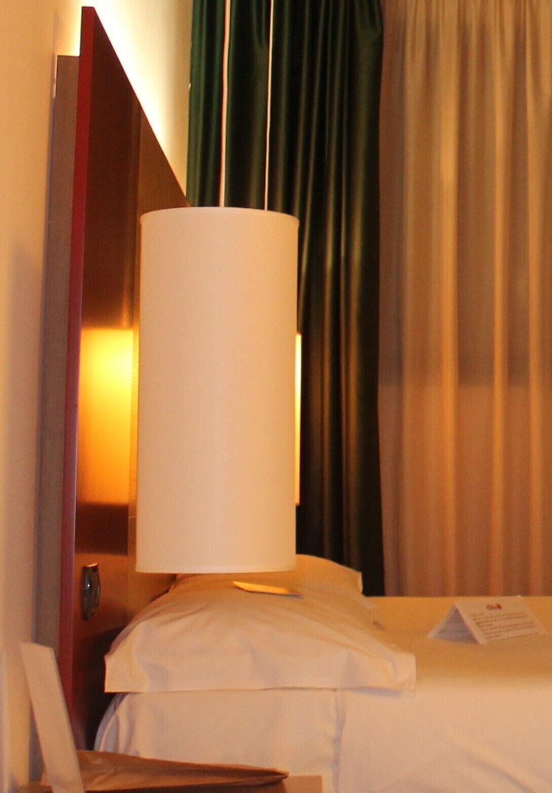 Ein Hotelzimmer mit Bett, Nachttisch, Lampe und Vorhängen.