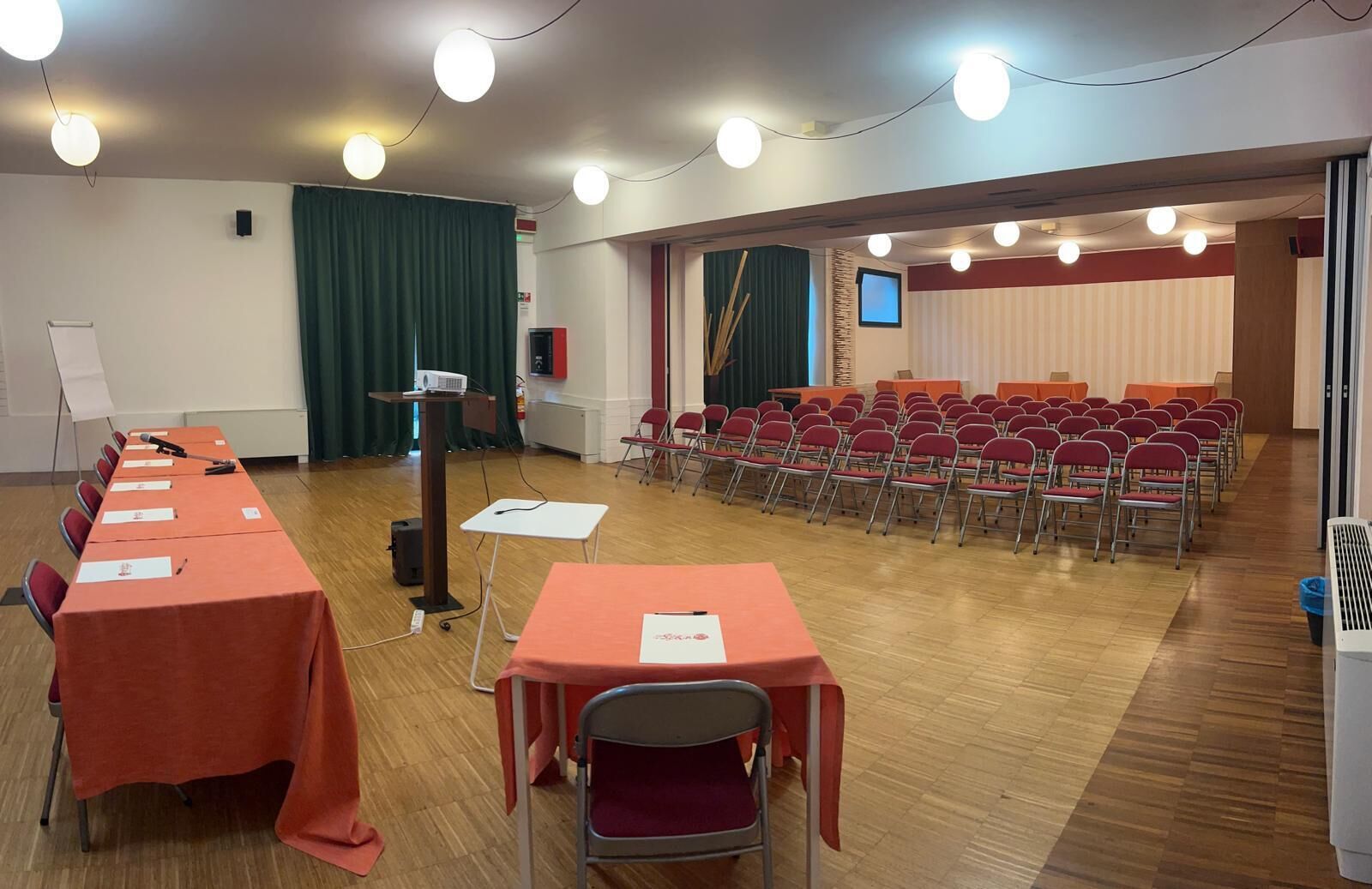 A conference room with rows of tables and chairs, a podium, and a stage with curtains.