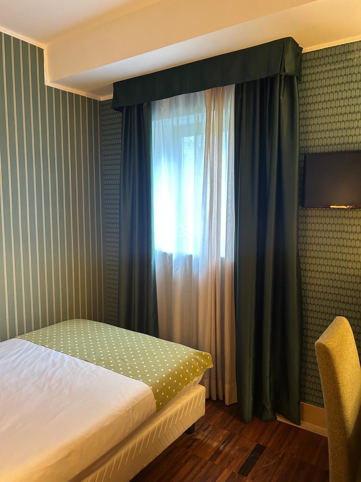 A hotel room with a bed, a television, and a window with curtains.