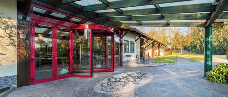 A covered entrance with a glass door, a circular stone pattern on the ground, and a pathway leading to a building.