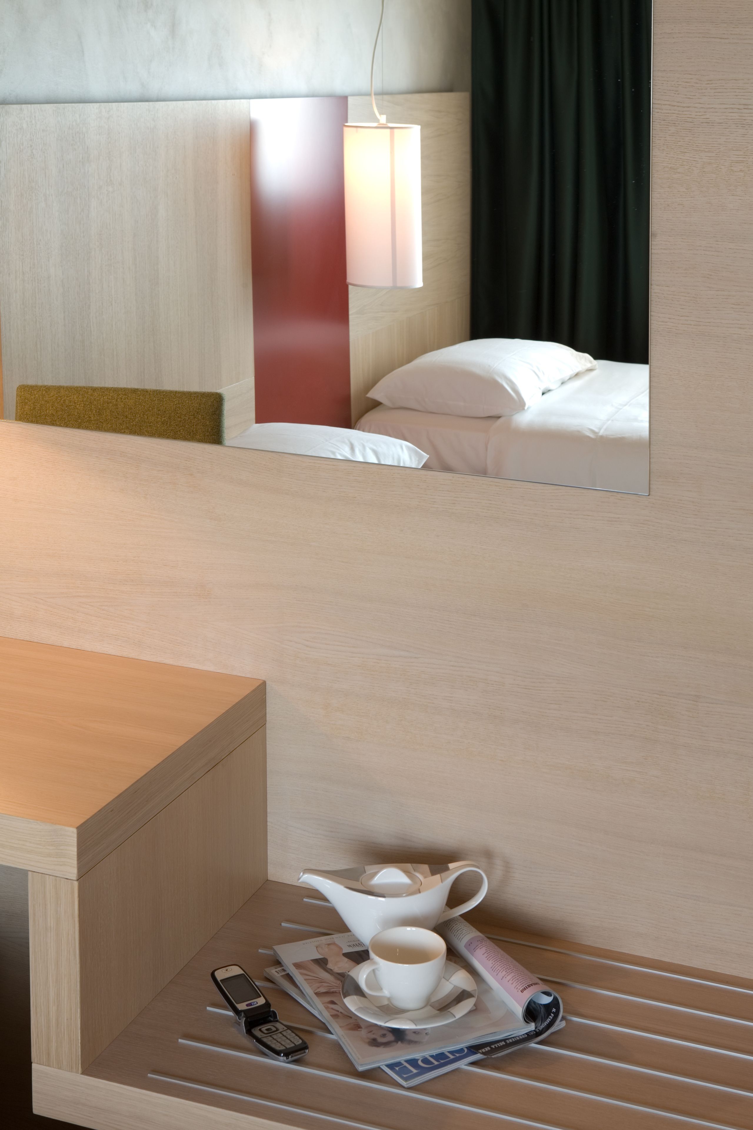 Una camera d'albergo con un letto, un comodino con una rivista, una tazza e un telefono.