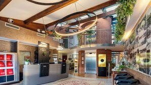 A hotel lobby with a reception desk, seating area, and a staircase leading to an upper level.