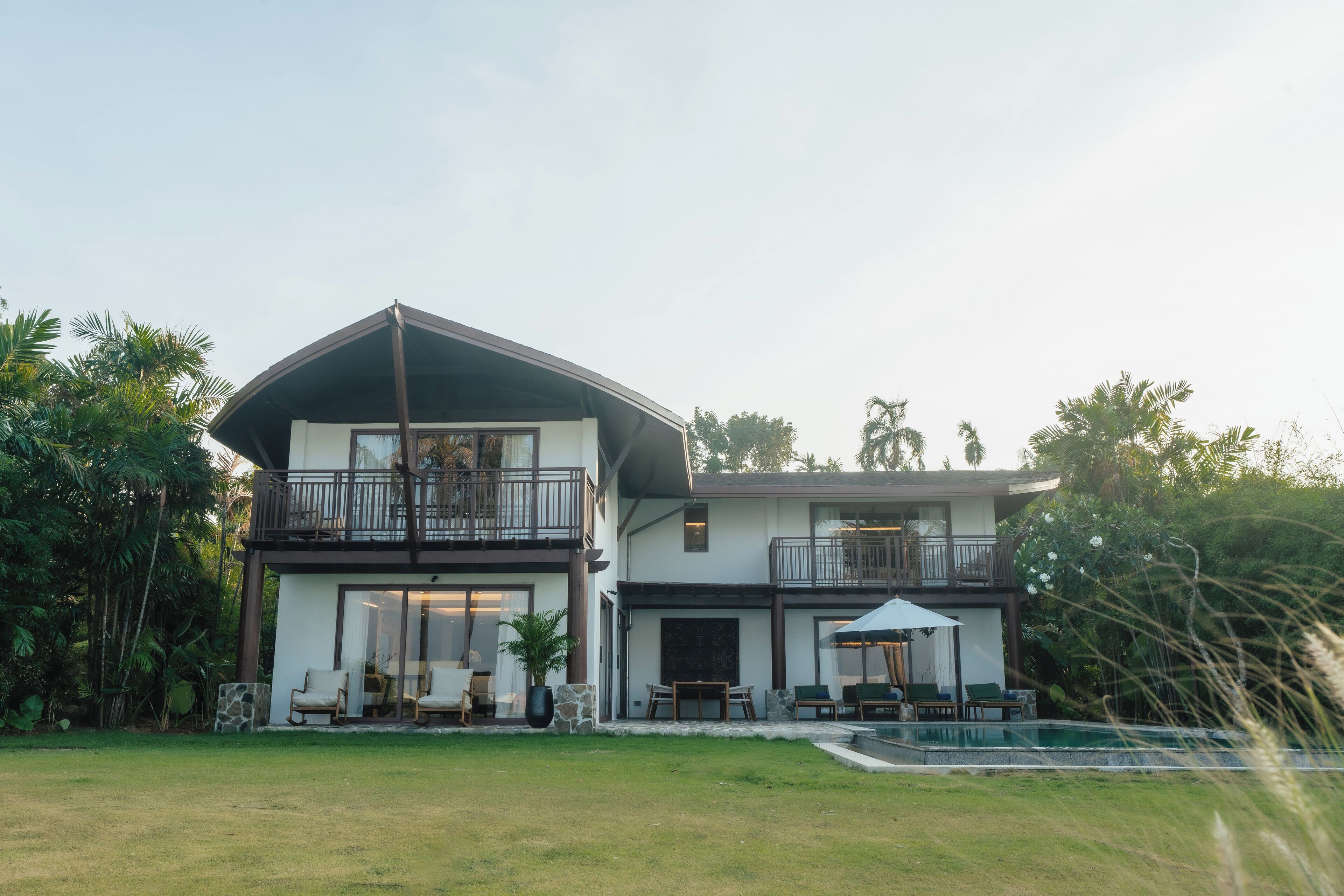 A two-story house with a balcony, a pool, and outdoor seating.
