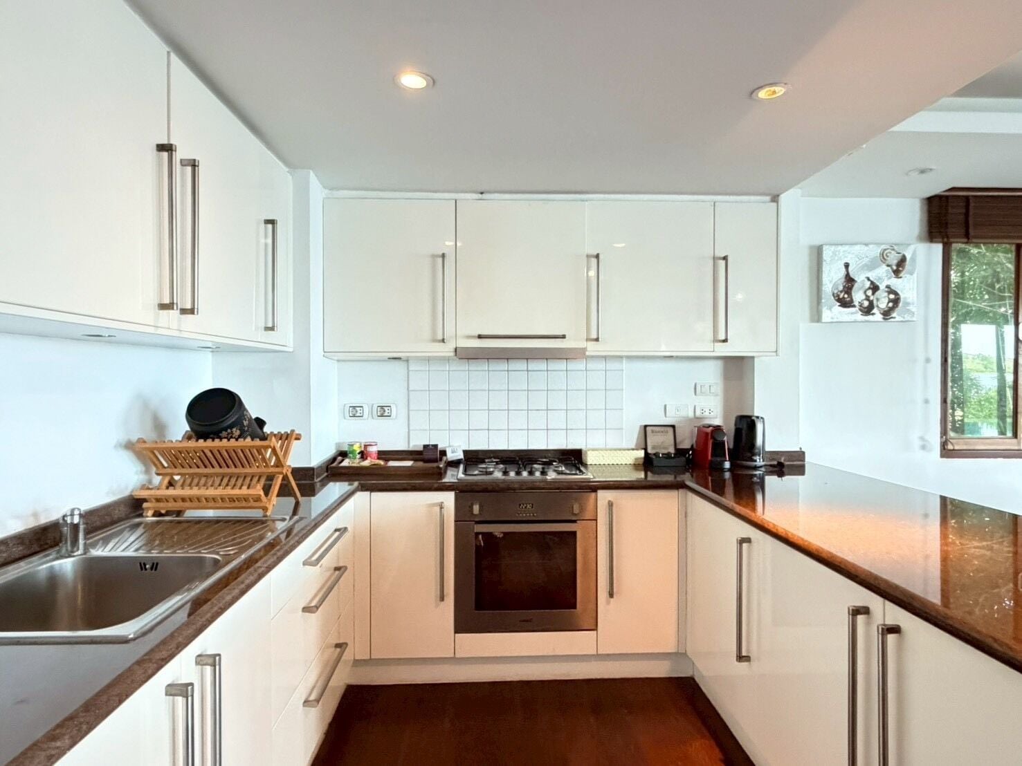 A modern kitchen with white cabinets, a stainless steel sink, a stove, and a coffee maker.