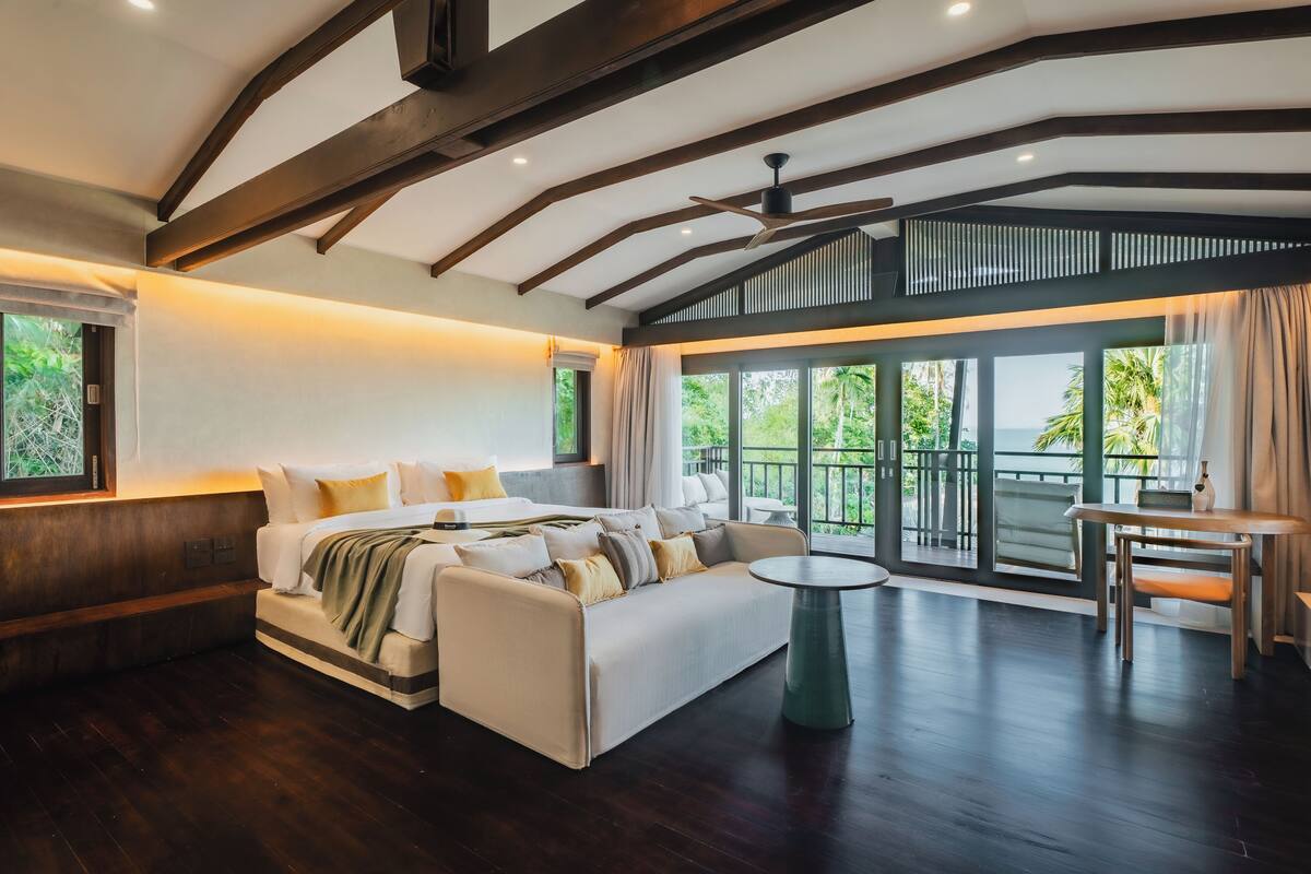 A spacious living area with a sofa, a small round table, and a balcony with large windows.