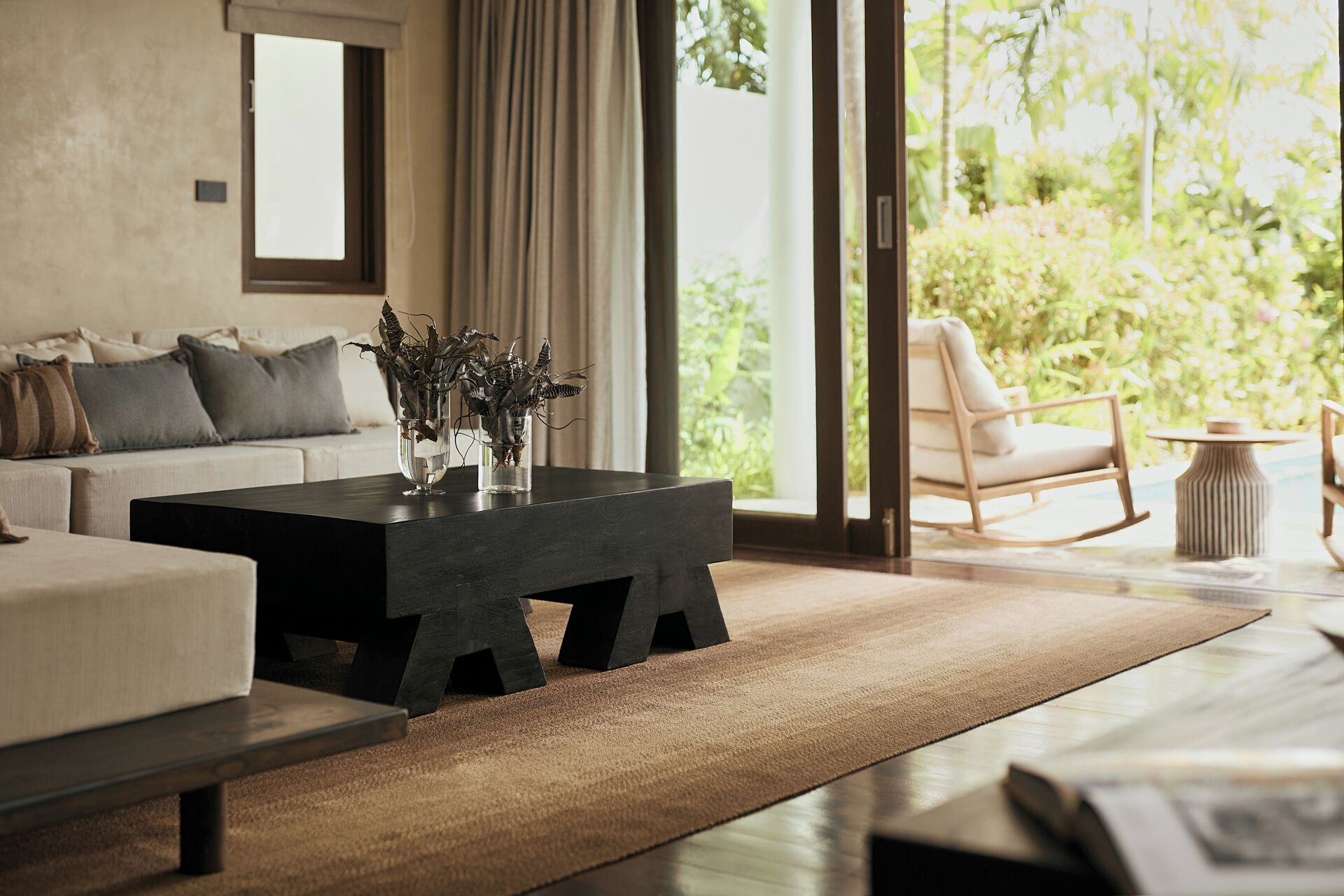 A modern living room with a sofa, coffee table, and a view of greenery outside.
