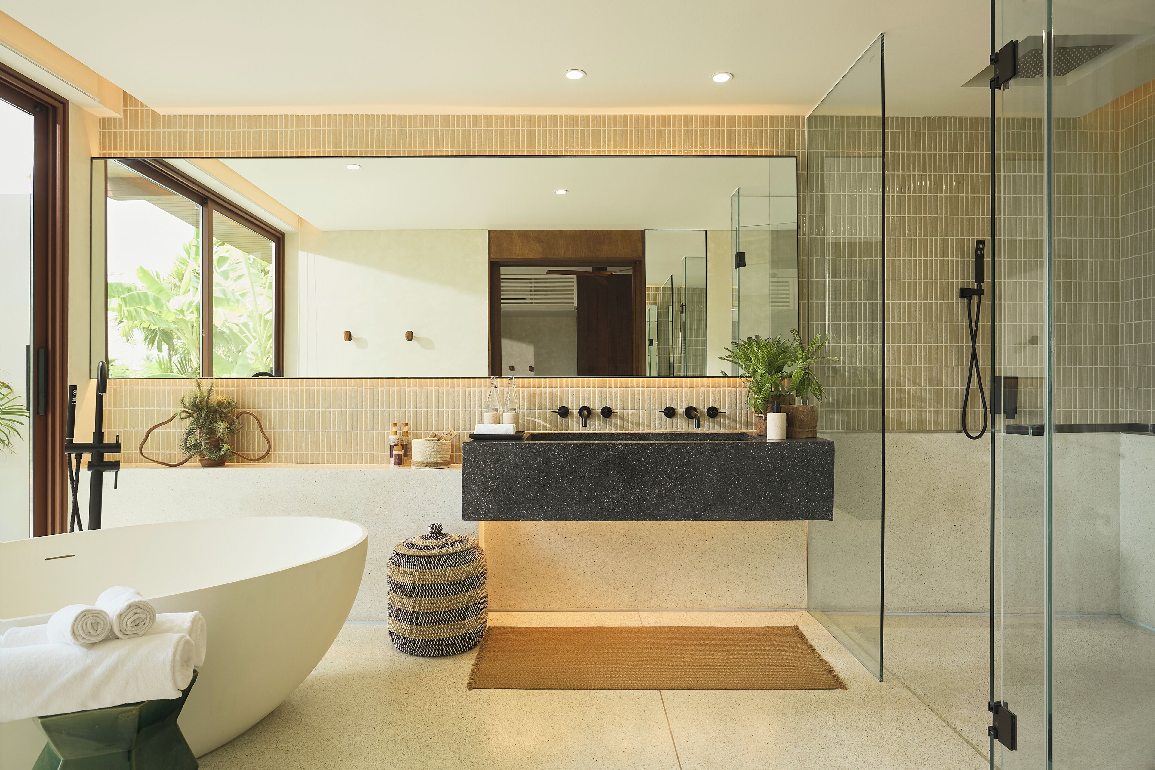 Un baño moderno con una bañera independiente, ducha con cabina de cristal y un espejo grande sobre el lavabo.