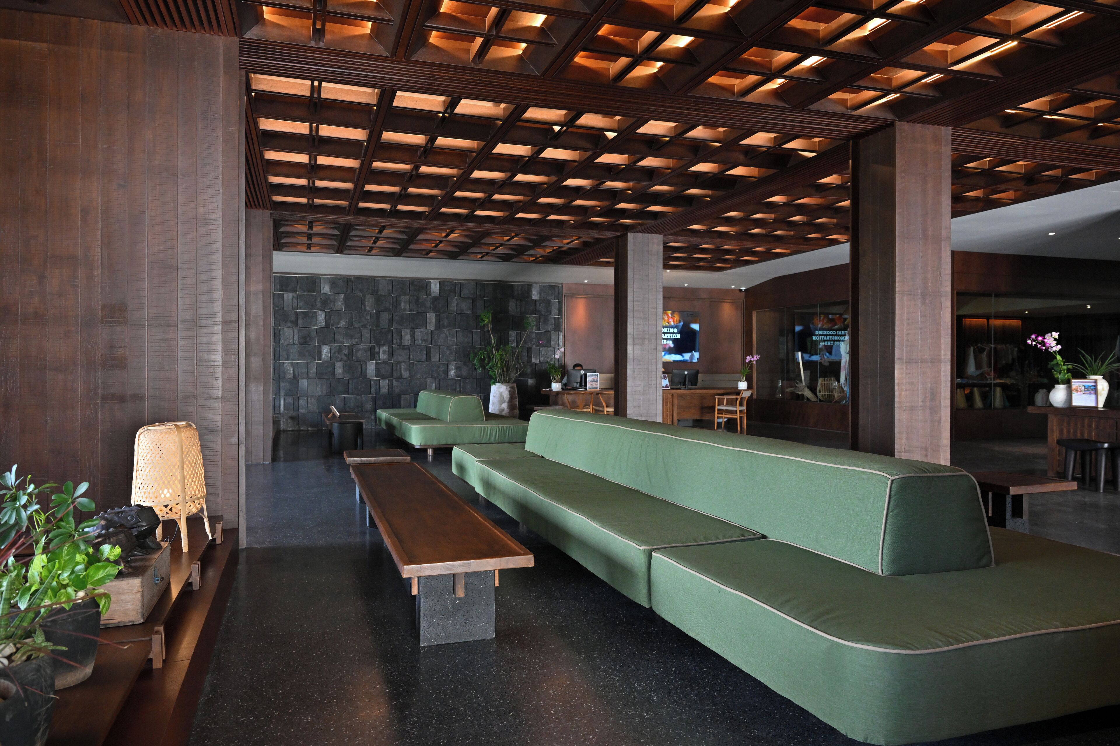 A modern lobby with a green sofa, wooden benches, and a stone wall.