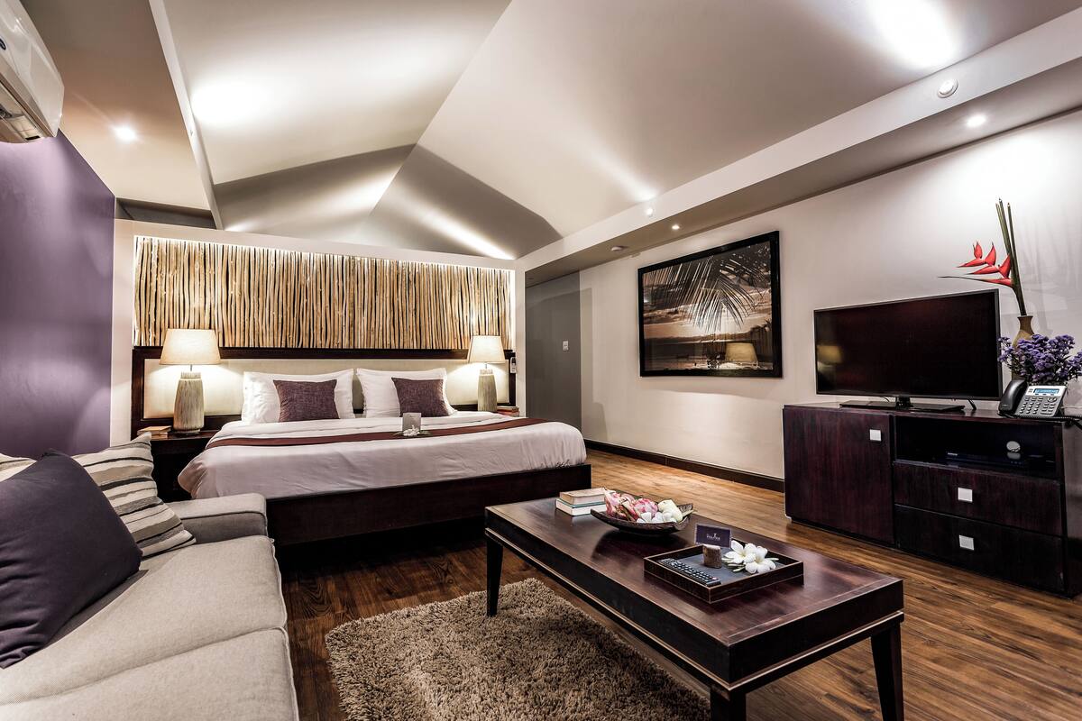 A modern hotel room with a large bed, a sofa, a coffee table, and a TV.
