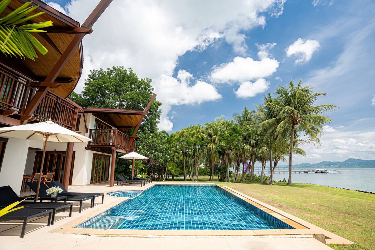 A pool area with lounge chairs and umbrellas, a wooden deck, and a view of the sea.