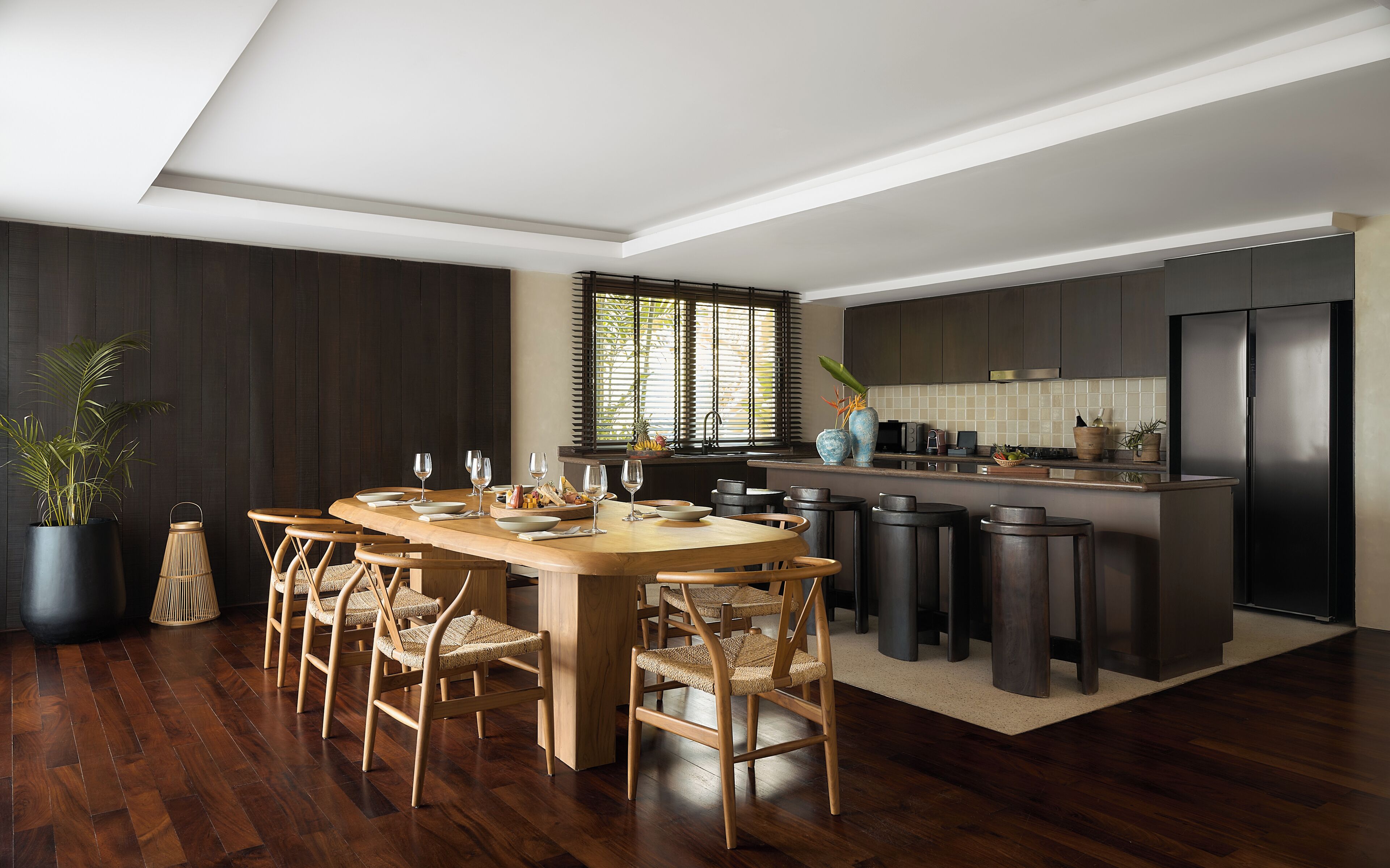 A modern kitchen with dark cabinetry, a wooden dining table, and bar stools.