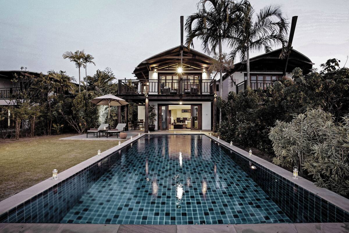A two-story house with a swimming pool, surrounded by tropical vegetation.