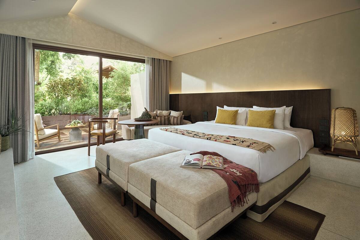 A modern hotel room with a large bed, a small table, and a seating area with chairs.